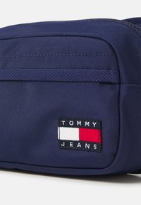 Borsa di tessuto blu navy con superficie testurizzata e chiusura con zip. Presenta una patch rettangolare con dettagli in rosso, bianco e blu.