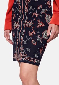 Knee-length navy skirt with intricate floral and paisley patterns in red and white, featuring a textured fabric and fitted design.
