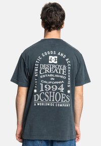 Szary t-shirt bawełniany w kolorze węgla drzewnego z dużym białym nadrukiem na plecach zawierającym tekst i logo, krótkie rękawy oraz luźny krój.