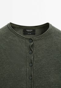 Olivengrøn hør henley-skjorte med rund halsudskæring, fem knappelukning og tekstureret strikket stof. Brandetiket synlig indvendigt.