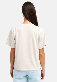 Μπεζ βαμβακερό t-shirt με κοντά μανίκια, στρογγυλή λαιμόκοψη, ίσια κοπή και καθαρό τελείωμα. Το ύφασμα φαίνεται απαλό και ελαφρύ.