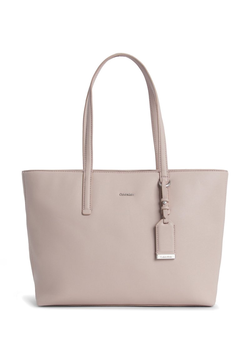 Beige tote bag fremstillet af glat læder, med to lange håndtag, et aftageligt mærke og et minimalistisk design. Logo vist på forsiden.