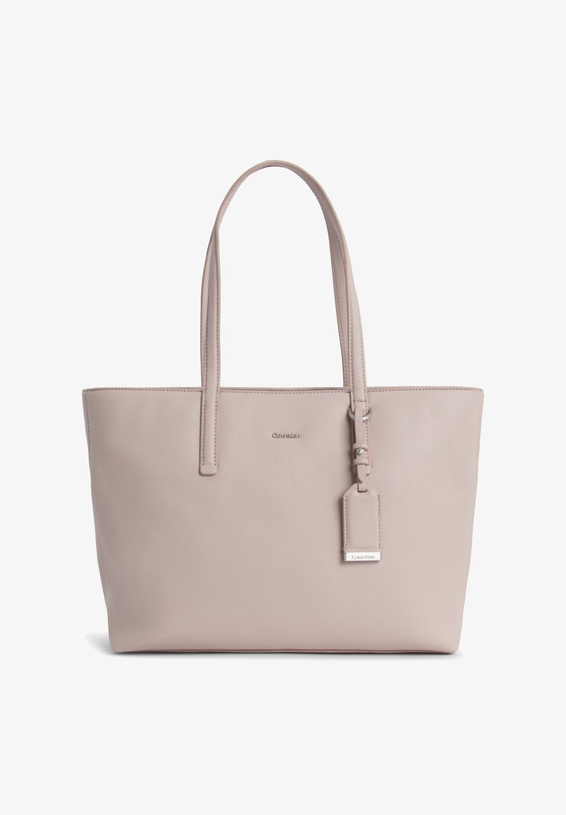 Beige tote bag fremstillet af glat læder, med to lange håndtag, et aftageligt mærke og et minimalistisk design. Logo vist på forsiden.