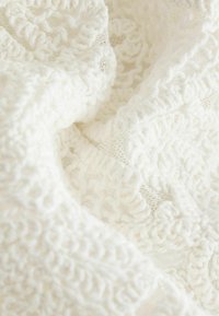 Tissu blanc texturé présentant un mélange de motifs tricotés et crochetés, doux et épais, avec des variations subtiles dans le tissage et les détails du design.