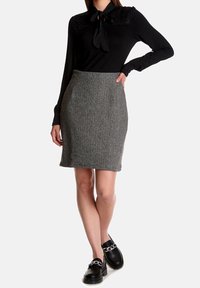 Maglietta nera a maniche lunghe con accenti in pizzo e un nodo al collo, abbinata a una gonna a matita in tweed grigio e mocassini neri con dettagli in catena.