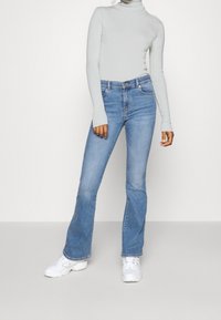 Pull en col roulé gris clair, ajusté, associé à un jean bleu évasé. Des baskets blanches complètent la tenue. Design simple et épuré sans embellissements.