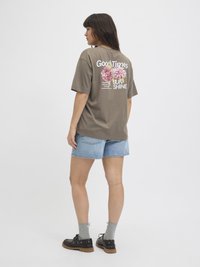 Grijze katoenen t-shirt met bloemenprint en tekst op de achterkant, gecombineerd met blauwe denimshorts. Gediend met grijze sokken en zwarte schoenen.
