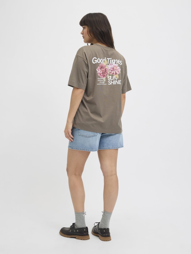 Grijze katoenen t-shirt met bloemenprint en tekst op de achterkant, gecombineerd met blauwe denimshorts. Gediend met grijze sokken en zwarte schoenen.
