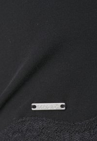 Tecido preto com uma textura suave, com uma borda rendada na parte inferior e um rótulo prateado gravado com "MAGIC®" anexado.