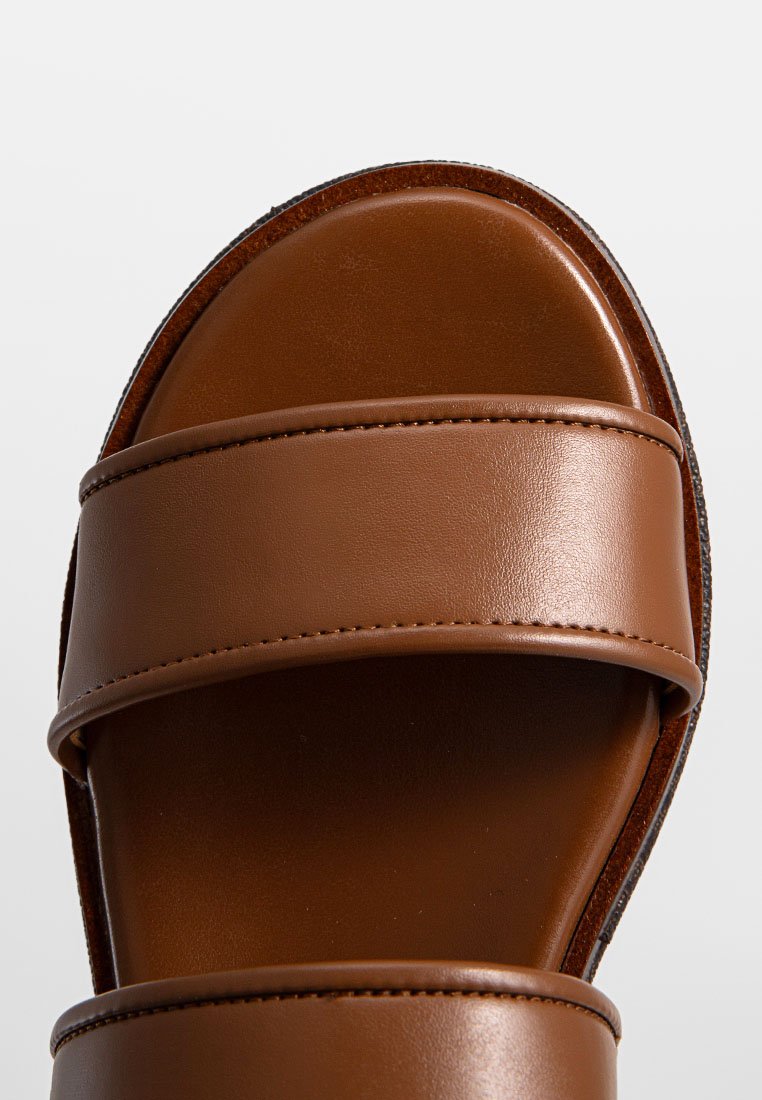 Sandali a scivolo in pelle marrone con due ampie cinturini regolabili, una texture liscia e una suola piatta con sottili dettagli di cucitura.
