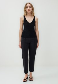 Schwarzes, geripptes Tanktop mit V-Ausschnitt, kombiniert mit maßgeschneiderten schwarzen Hosen. Das Outftit wird durch schwarze Flip-Flops ergänzt.