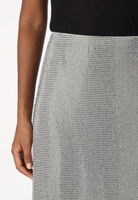 Silver sequined skirt with a fitted waistband, featuring a shimmering, textured surface with a grid pattern and a smooth fabric feel.