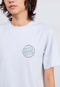 T-shirt in cotone azzurro chiaro con un grafico circolare con la scritta "Santa Cruz" e stelle decorative, maniche corte e scollatura rotonda.