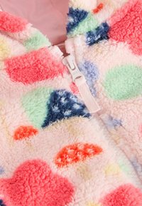 Fleecetröja med dragkedja med livliga prickar i rosa, rött, grönt, gult och blått på ett mjukt, strukturerat tyg. Vit dragkedja.