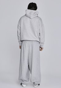 Grauer Baumwoll-Hoodie mit Kapuze, lockerer Passform und gerippten Säumen, kombiniert mit passenden grauen, locker sitzenden Sweatpants. Einfaches Design, keine Muster.