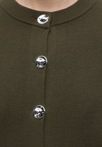 Gros plan d'un cardigan en tricot vert foncé avec trois boutons ronds argentés brillants fermés sur le devant.