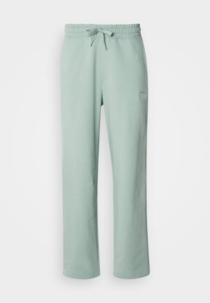 Light green sweatpants with an elastic waistband and drawstring. Features side pockets and a small logo patch on the front. Smooth texture.