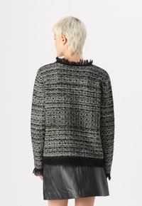 Svart og hvit teksturert strikkegenser med frynsete kanter, med rund hals og oversized passform. Kombinert med et sorte skinnskjørt.