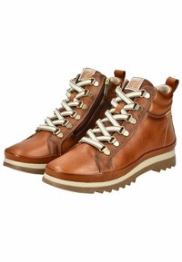 Bottes chelsea en cuir marron avec une finition texturée, dotées de lacets blancs, de crochets dorés et d'une fermeture éclair latérale, reposant sur une semelle en caoutchouc crème.