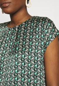 Lyhythihainen mekko musta-valko-teal-kuvioinnilla, joka muistuttaa faneja, valmistettu sileästä kankaasta, joka on pehmeästi kiiltävä.