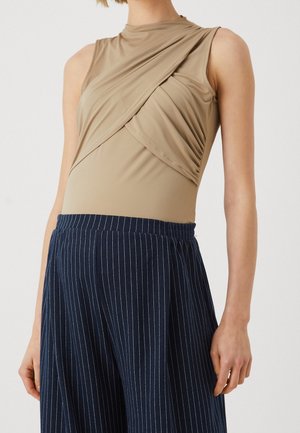Beige ærmeløs bodysuit med rynket stofdetalje. Parret med navy vertikalt stribede vide bukser med elastisk talje.