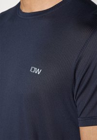 Mørkeblå kortærmet t-shirt lavet af tekstureret stof med en rund halsudskæring og et lille hvidt logo på brystet.