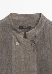 Hnědý texturovaný lněný oděv s stojatým límcem a dvěma viditelnými knoflíky u krku, označený Massimo Dutti, vyrobený v Číně.