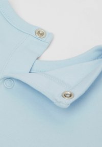 Svetlemodrý límec oděvu s jemnou texturou. Obsahuje patentku se stříbrným kovovým akcentem a má čistý, jednoduchý design.