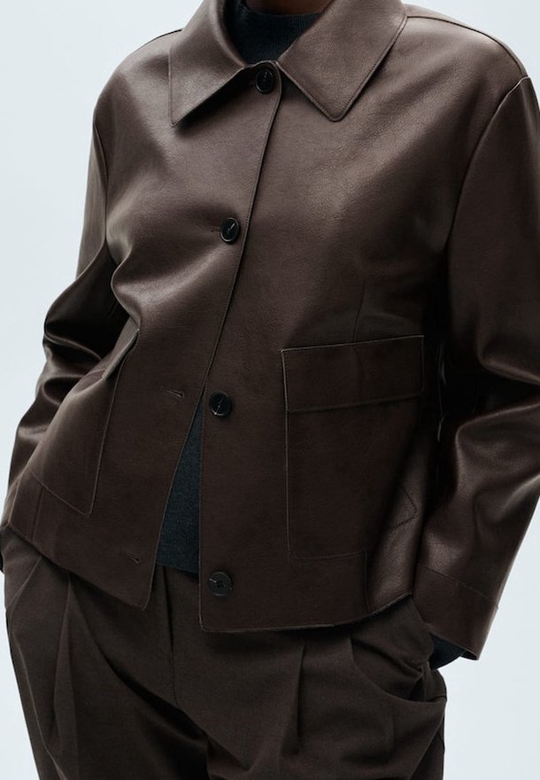 Brązowa skórzana kurtka z klasycznym kołnierzem, guzikami z przodu i pojedynczą naszywaną kieszenią, cechująca się gładką fakturą i dopasowanym krojem.