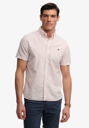 Chemise à manches courtes avec boutons, de couleur rose clair avec une finition texturée, dotée d'un petit logo brodé sur la poitrine et de boutons jaunes.