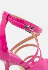 Sandale à talons hauts en cuir verni rose vif avec plusieurs brides et une boucle argentée gravée des initiales "MK".