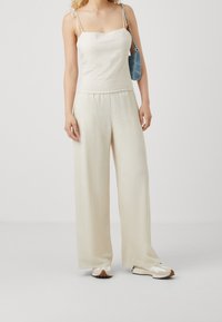 Top de tirantes finos en color crema claro, combinado con pantalones amplios con pliegues. Calzado casual en una paleta de colores beige y blanco. Bolso de hombro corto.