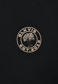 Čierne tričko s krátkym rukávom s kruhovým logom v svetlo béžovej farbe, zobrazujúcim strom a nápismi "BLK VIS" a "EST. 2013".
