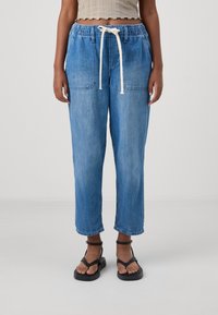 Jasnoniebieskie, luźne dżinsowe joggery z elastycznym pasem i białym sznurkiem. Zawierają dwie przednie kieszenie i skrócony dół.