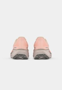 Chaussures de trail running avec une tige en mesh rose, des accents beiges et une semelle grise rembourrée ; semelle extérieure texturée pour adhérence et stabilité.