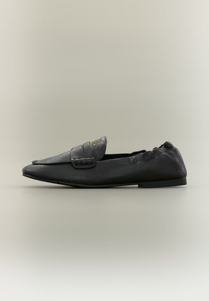 Mocassin en cuir noir à enfiler, talon bas, dos élastiqué et bride décorative sur le dessus avec lettres dorées.