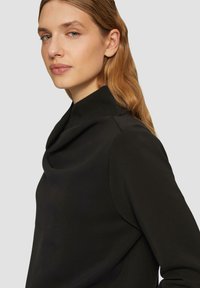 Schwarzes Top mit Kapuze, das sich durch eine glatte Textur, lange Ärmel und eine taillierte Silhouette auszeichnet. Dezente Nähte an den Schultern.