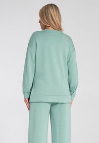 Miętowa bluza typu sweatshirt o luźnym kroju, z opadającymi ramionami i ściągaczami. Posiada gładką teksturę i prosty dół.