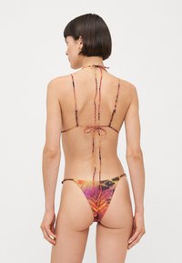 Bikini med et livlig abstrakt mønster i oransje, rosa og gult. Den har tynne, glidningsfrie stropper og minimal dekning på ryggen med justerbare knytninger.