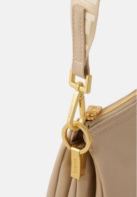 Borsa in nylon beige con hardware dorato, dotata di tracolla removibile e chiusura con zip. Dettagli notevoli includono un'etichetta con logo e cuciture.