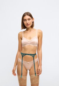 Lichtroze kanten bralette met verstelbare bandjes, gecombineerd met kanten slips en een teal kousenband, voorzien van klassieke hardwaredetails.