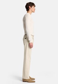 Pantaloni in cotone beige con una vestibilità dritta e dettagli visibili sulle tasche posteriori, abbinati a un top crema a maniche lunghe e stivali alla caviglia in suede beige.