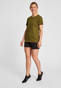 Oliven grøn bomulds-T-shirt med korte ærmer og rund halsudskæring, parret med sorte shorts. Looket afsluttes med sorte atletiske sko.
