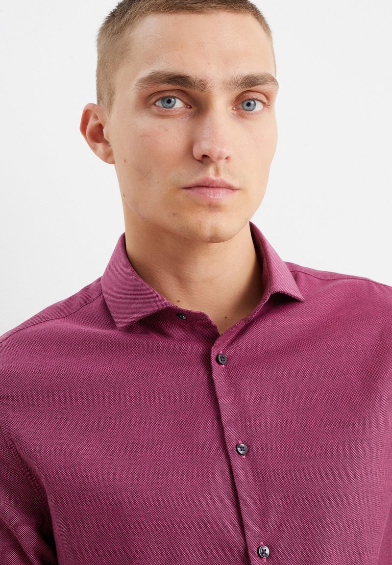Casual kastanjebruine button-up shirt met een gestructureerde stof, kraag en donkere knopen. Close-up weergave die de stofdetails en de vorm van de kraag toont.