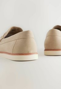 Beige Wildlederschuhe mit einem abgerundeten Absatz und einer weißen Gummisohle. Verfügt über eine beige gestickte Naht und einen Holzauschnitt entlang der Sohle.
