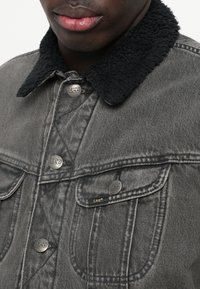 Geacă din denim gri, având un guler din fâș sintetic negru, nasturi din metal de culoare argintie și sigla Lee pe zona pieptului și pe buzunare.