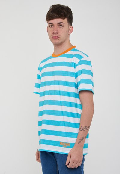 Maglietta a maniche corte a righe turchese e bianche con scollatura arancione e logo "MOSCHINO SWIM" vicino all'orlo. Modello seduto che mostra la vestibilità.