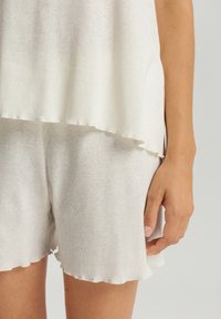 Top grigio chiaro in maglia morbida con orlo arrotondato, abbinato a pantaloni corti leggeri coordinati con un bordo a onde. Fit semplice e rilassato.