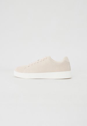 Beige Wildlederschuhe mit weißen Gummisohlen, runder Zehenform und sechs Ösen für die Schnürsenkel. Glatte Textur mit minimalistischem Design.