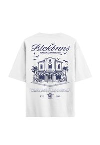 Witte katoenen t-shirt met een blauwe afbeelding van een gebouw met palmbomen en vogels, met de tekst "Blckbnns Marina Moments" erboven en eronder.